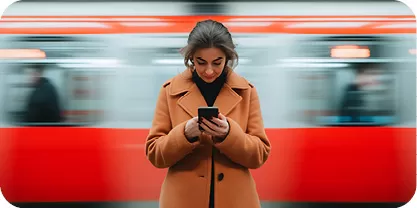 Young woman standing in front of a moving red train looking at her phone. 